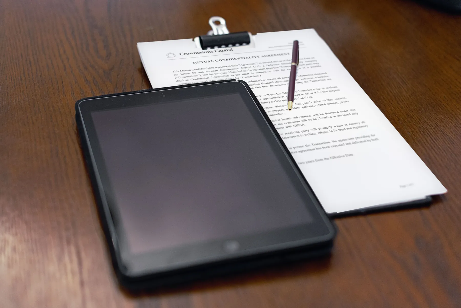 A mutual confidentiality agreement on Crownestone Capital letterhead, clipped to a board beside a tablet on a wooden table