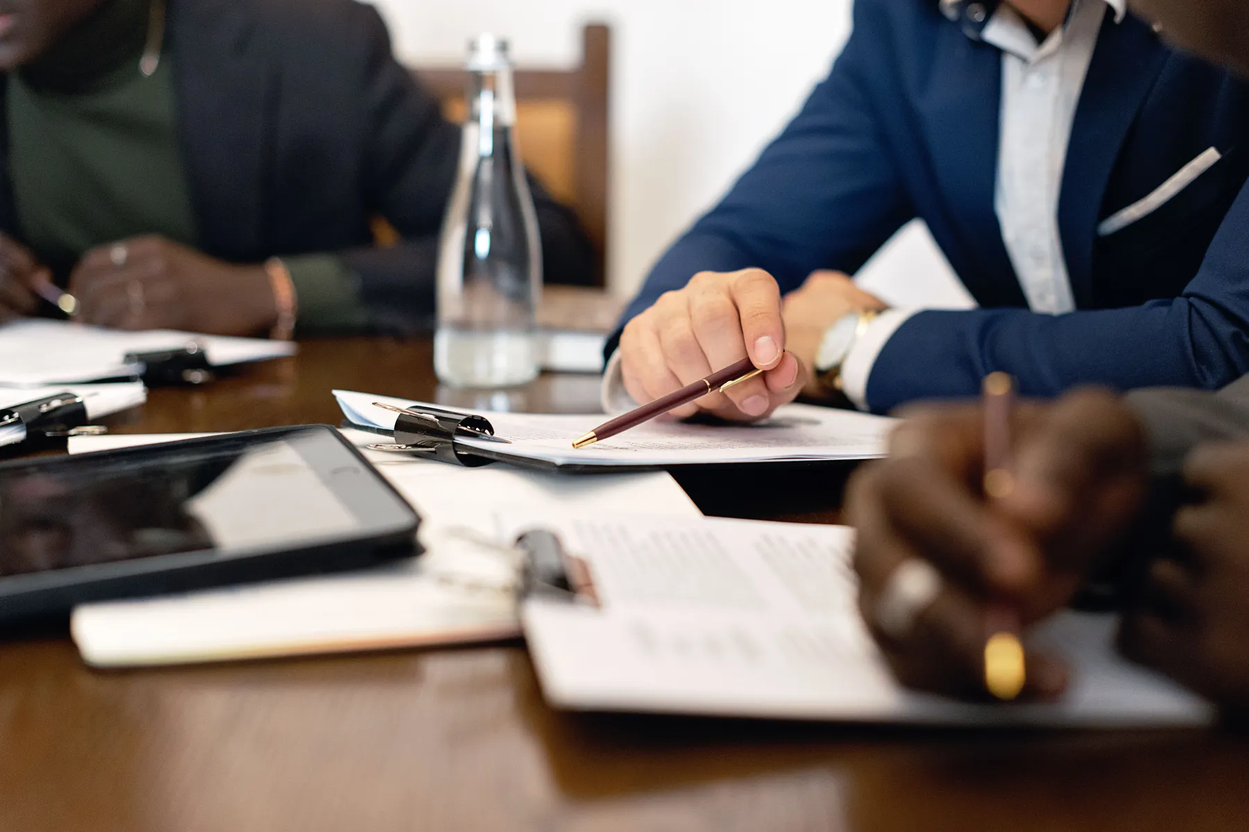 Three people at a conference table reviewing clipped documents, one pointing with a pen