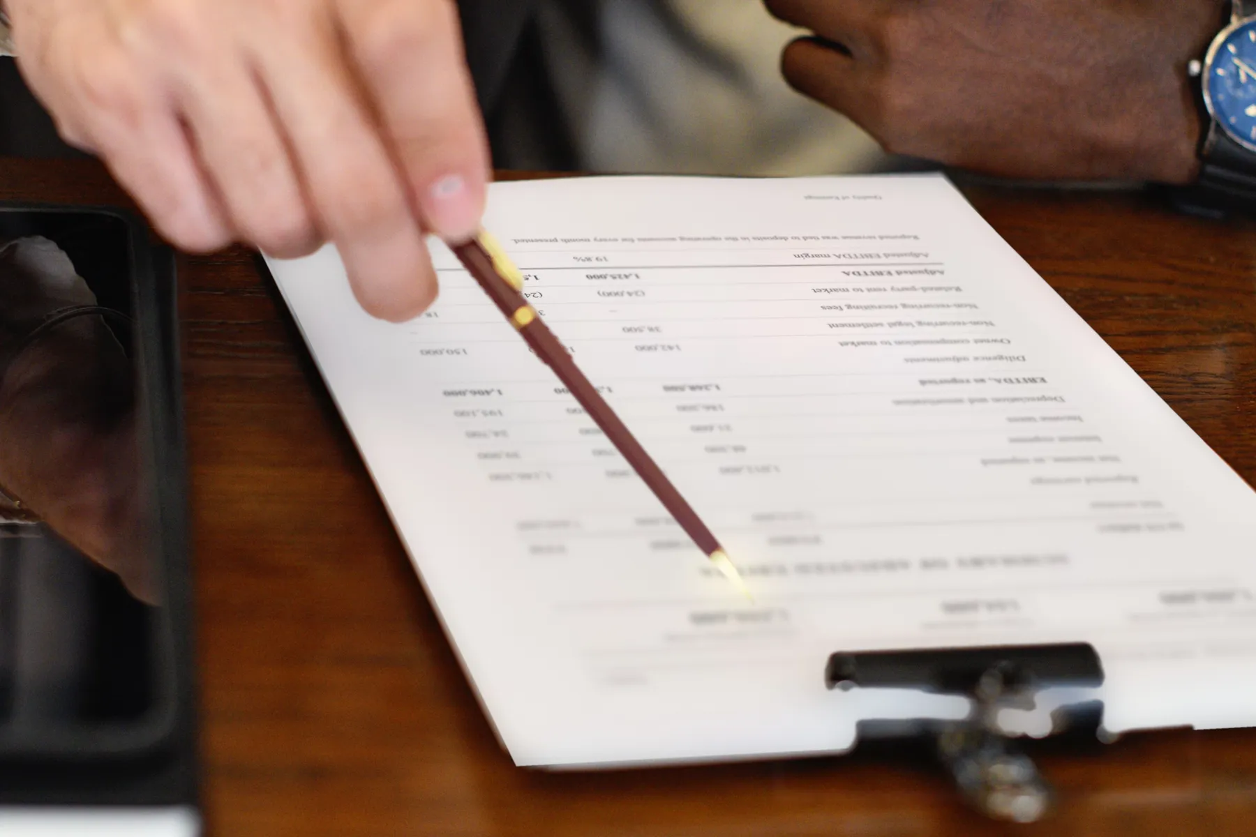 A pen pointing at the adjusted EBITDA on a quality of earnings summary