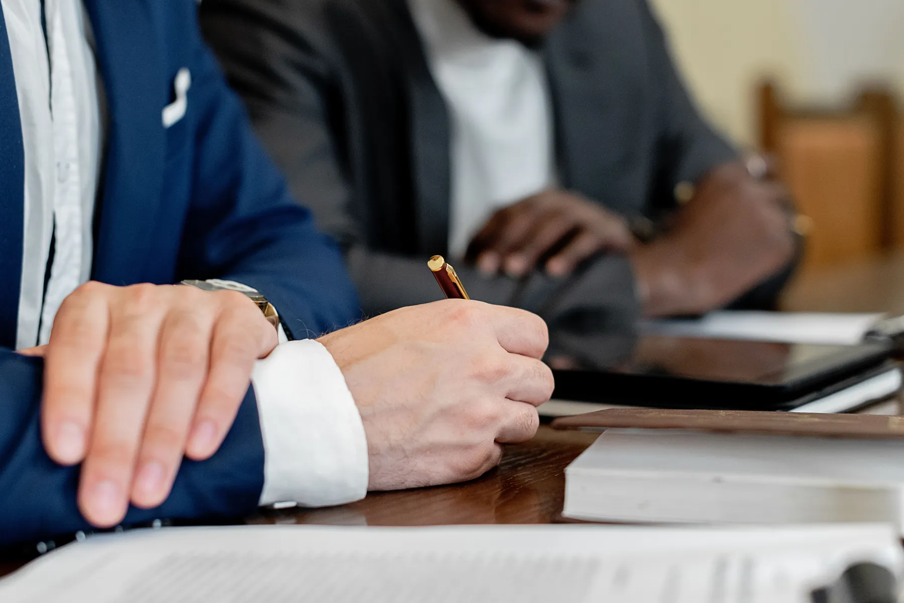 Two people in suits at a table, one signing a document