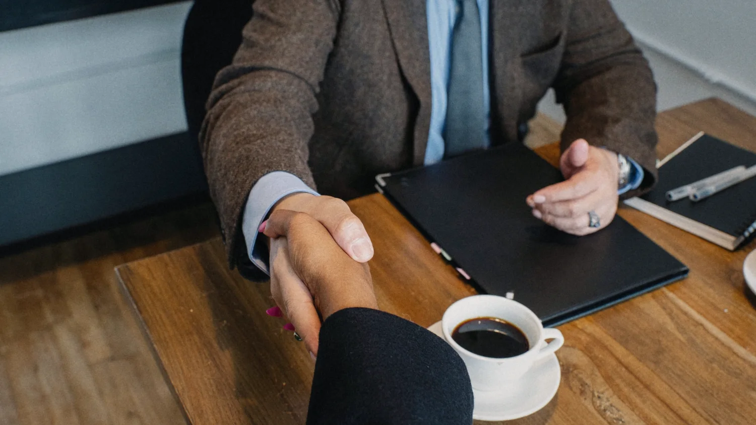 A handshake across the table, beside a cup of coffee